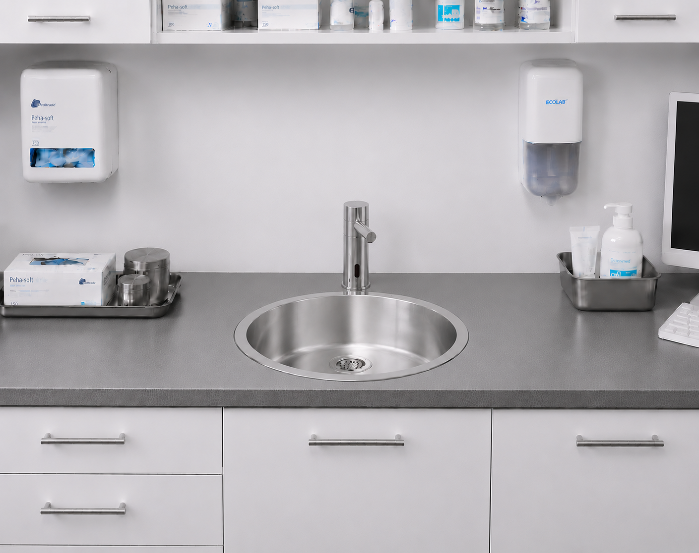 Modernes Edelstahlwaschbecken in einem sauberen, organisierten medizinischen Arbeitsbereich mit Hygieneartikeln und -geräten.